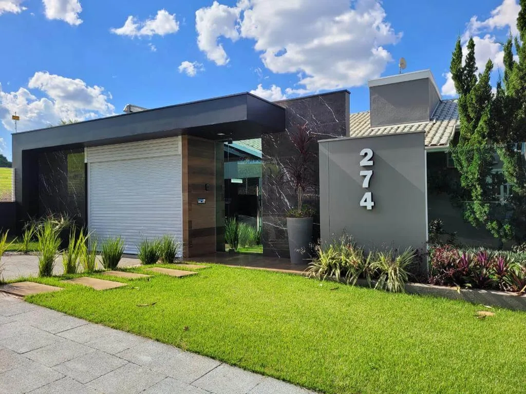Casa térrea contemporânea com portão de enrolar branco integrado à fachada, entre o gramado e a entrada social