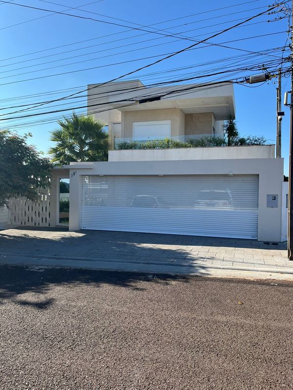 Portão de enrolar branco com lâminas perfuradas em cima e fechadas embaixo, em casa com palmeiras