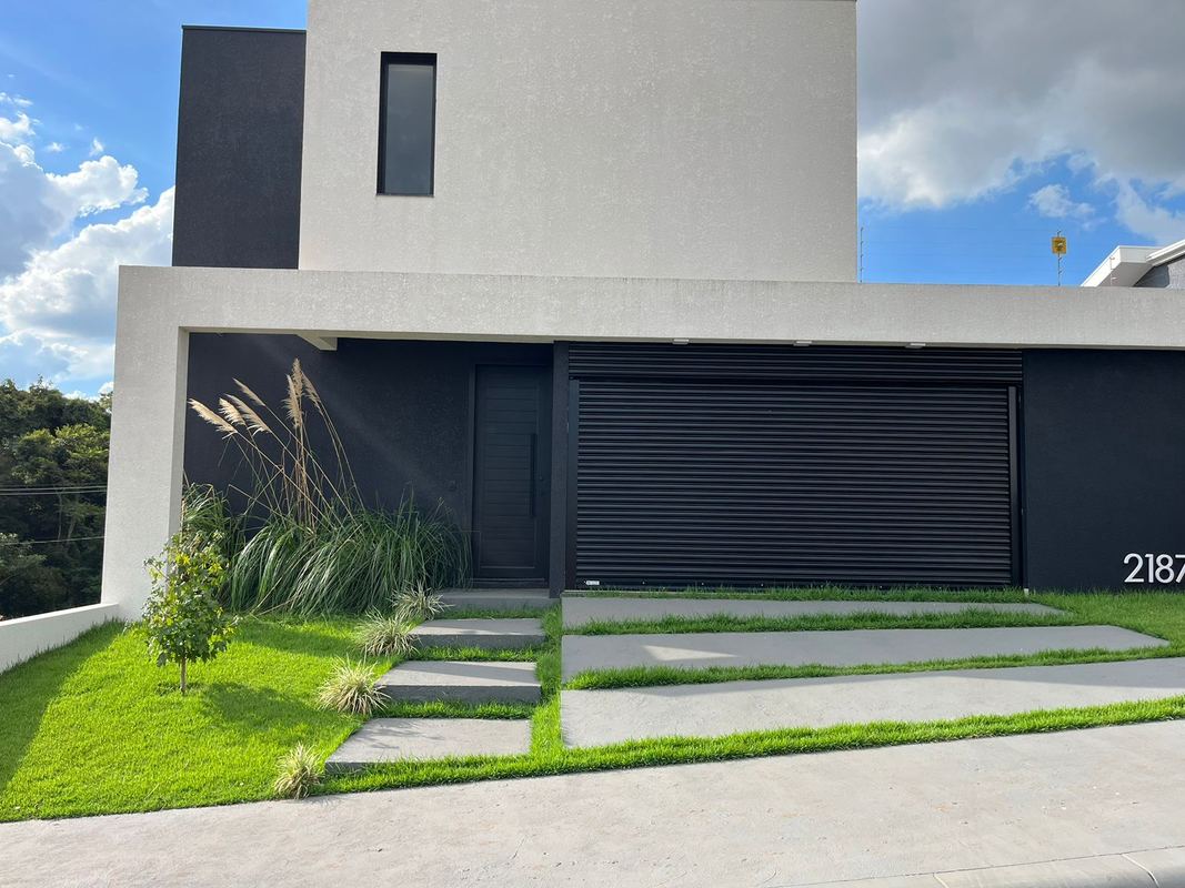 Portão de enrolar preto em casa contemporânea branca e preta, com gramado e jardim frontal