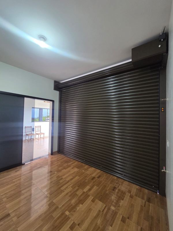 Portão de enrolar preto visto de dentro da garagem, com o mecanismo recolhido no alto e o piso livre