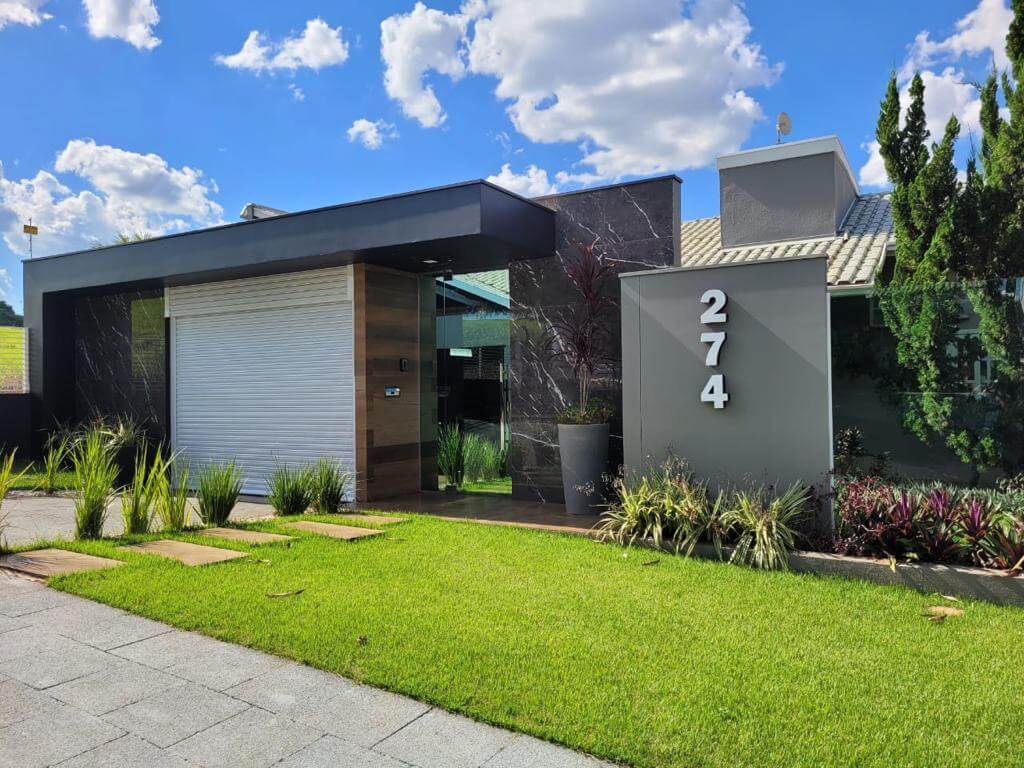 Casa térrea contemporânea com portão de enrolar branco integrado à fachada, entre o gramado e a entrada social